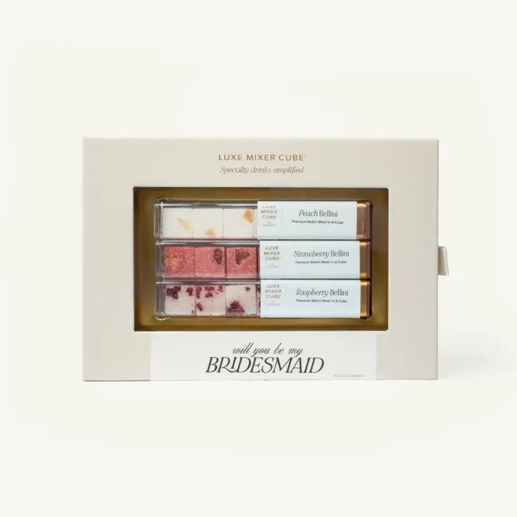 A boxed set of Luxe Mixer Cubes chocolates with a clear window showing four assorted chocolate pieces. The cream-colored box has gold text reading 'LUXE MIXER CUBES' and a white banner at the bottom that says 'will you be my BRIDESMAID'.